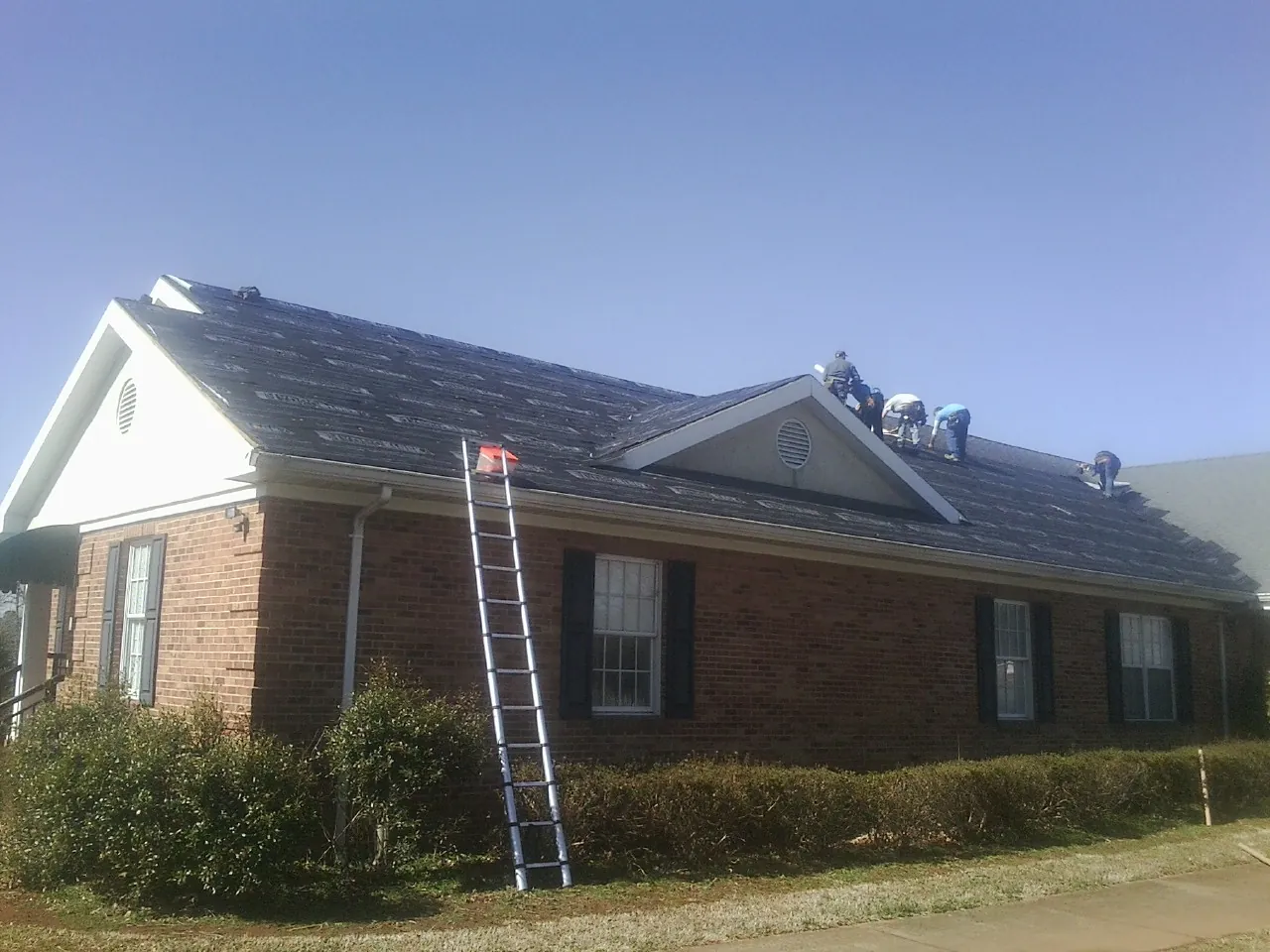 Crew tearing shingles off a brick ranch roof with a ladder set — Metal Roof Repair work by our crew in Erie